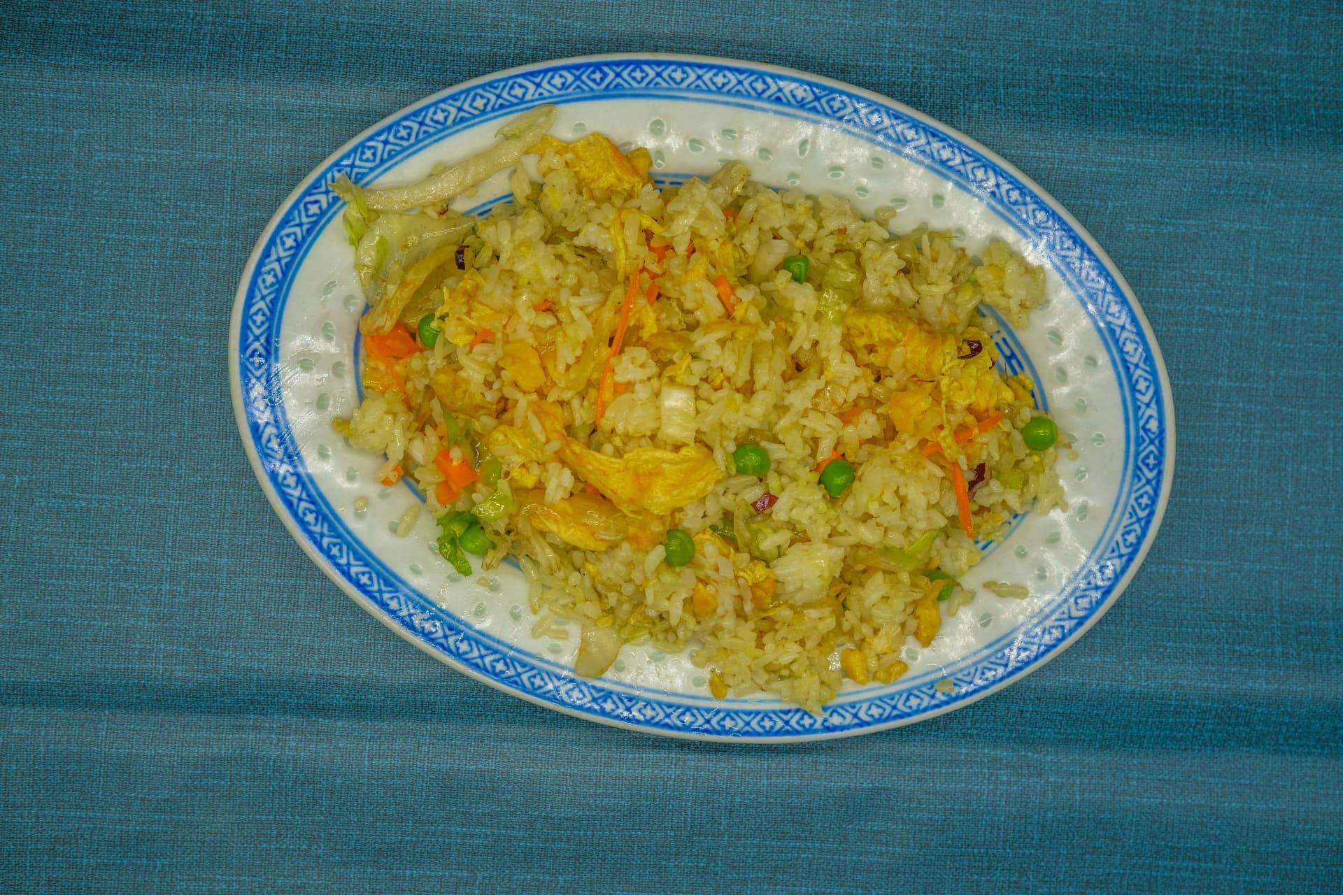 Arroz frito con huevo, guisantes y zanahoria en plato ovalado azul y blanco