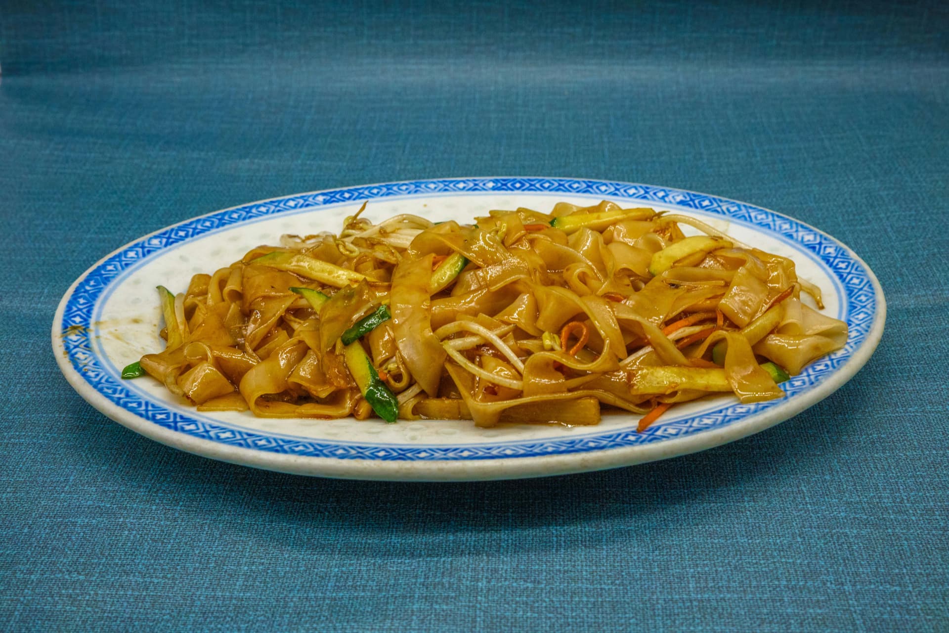 Fideos de arroz anchos salteados con brotes de soja y verduras en plato azul y blanco